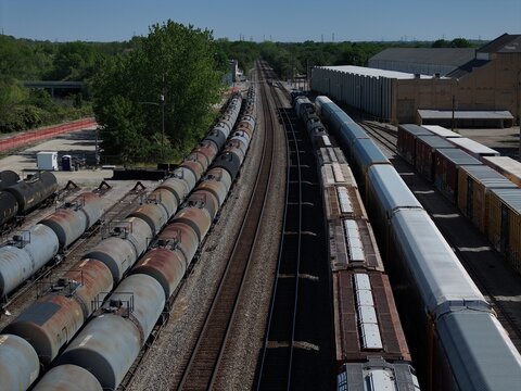 Aerial view of freight trains and tank cars on parallel tracks surrounded by industrial buildings and green trees Cincinnati, OH, United States.