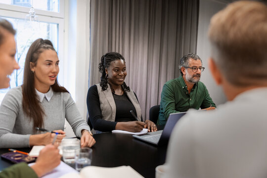 Smiling female business expert sitting with colleagues during meeting in office
