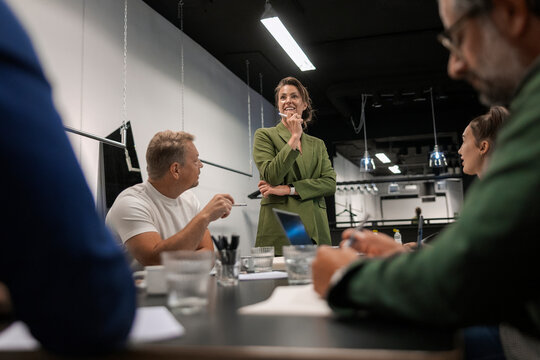 Low angle view of smiling female entrepreneur explaining strategies to colleagues in office conference room