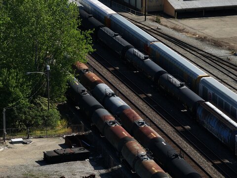Aerial view of freight train cars and tanker cars on parallel tracks next to a lush green tree in Cincinnati, OH, United States.