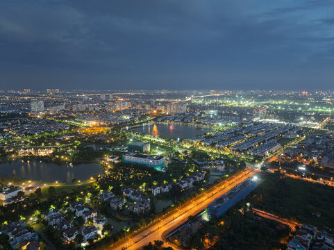Night aerial panorama capturing illuminated roads, lakes, and upscale residential districts in Long Bien, Hanoi beneath dramatic storm clouds.