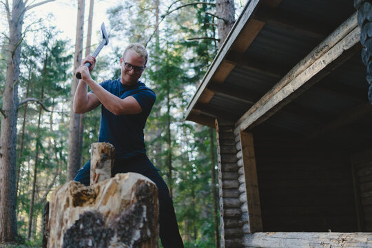 Man cutting wood log with axe near fireplace in forest