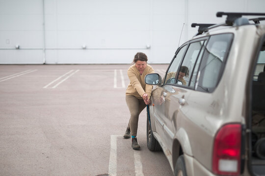 Full length of woman pulling lug wrench while changing flat tire of car