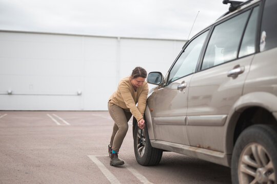 Full length of woman pulling lug wrench while changing flat tire of car in parking lot