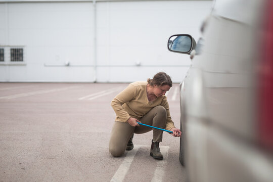 Woman crouching while changing flat tire of car with lug wrench in parking lot