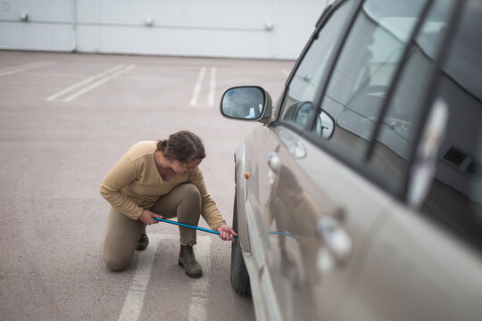 High angle view of woman crouching while changing flat tire of car with lug wrench in parking lot