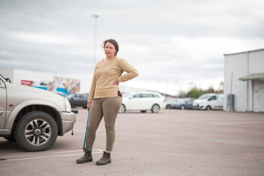 Portrait of tired woman holding lug wrench while standing with hand on hip in parking lot