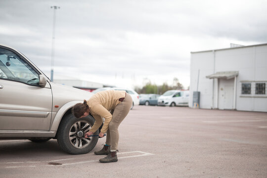 Full length of woman bending and fastening tire nut of with lug wrench in parking lot