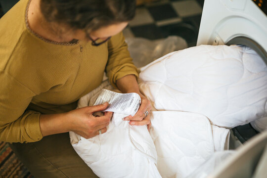 High angle view of woman reading instructions before putting duvet in washing machine