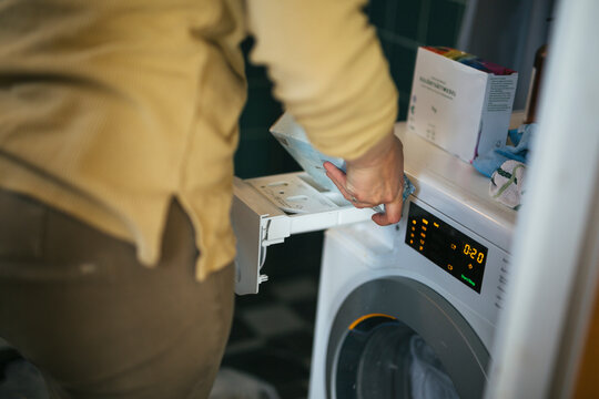 Midsection of woman putting laundry detergent in washing machine