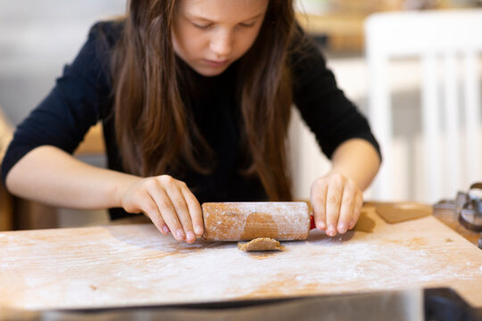 Focused girl rolling gingerbread cookie at home