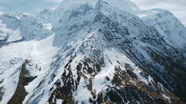 A breathtaking aerial view captures the snow-covered peaks and rugged ridges of a massive Himalayan mountain in Nepal under a hazy sky.