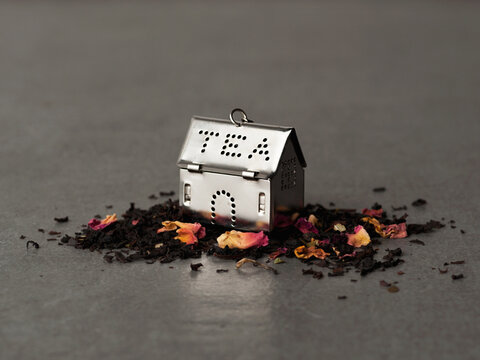 Shot of house-shaped silver tea infuser on pile of loose leaf tea