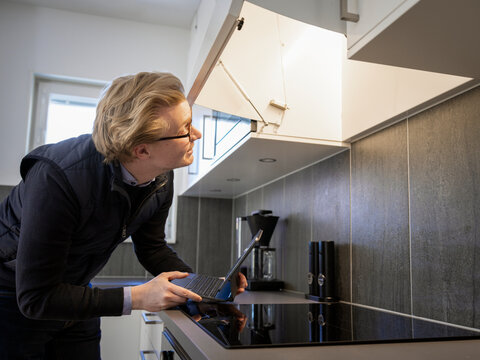 Male technician examining chimney while holding laptop in kitchen at home