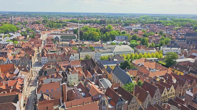 Scenic rooftop view of a historic city center with orange tile roofs, cathedral tower, cobblestone streets, traditional buildings, trees, and sunny travel destination skyline view.