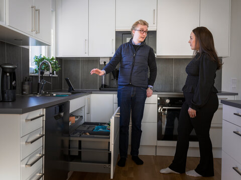 Male maintenance engineer explaining dishwasher problems to homeowner while standing in kitchen