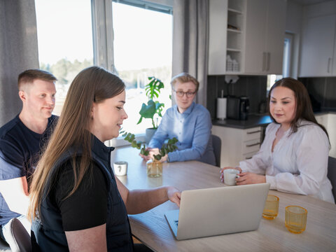 Smiling female building contractor explaining plan on laptop to family members at home