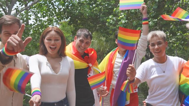 Pride and LGBTQ concept. A group of LGBTQ people dressed up, carrying rainbow signs and flags, dance and celebrate happily at a Pride festival event in the park.