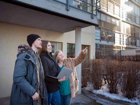 Smiling female property caretaker holding laptop listening to woman pointing while standing outside house