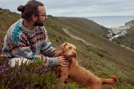 Long haired man spending leisure time with dog while sitting on grass