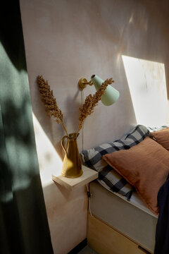 Vase of dried wheat stalks near wall sconce on floating nightstand near bed