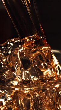 A jet of whiskey with splashes flows into a glass of ice. Against a dark background. Filmed is slow motion 1000 fps.