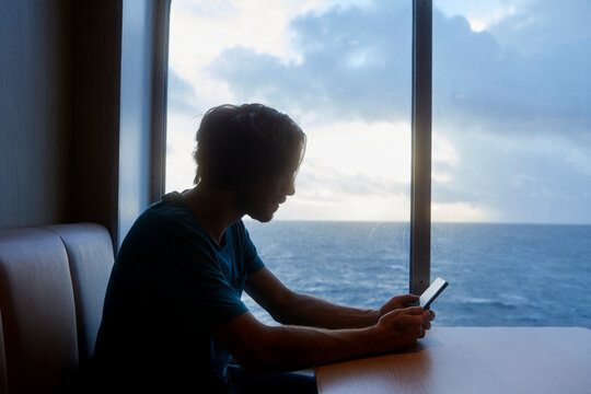 Man using smart phone while sitting near window on seat in ferry
