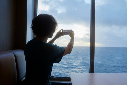 Rear view of man photographing sea view through smart phone while traveling in ship
