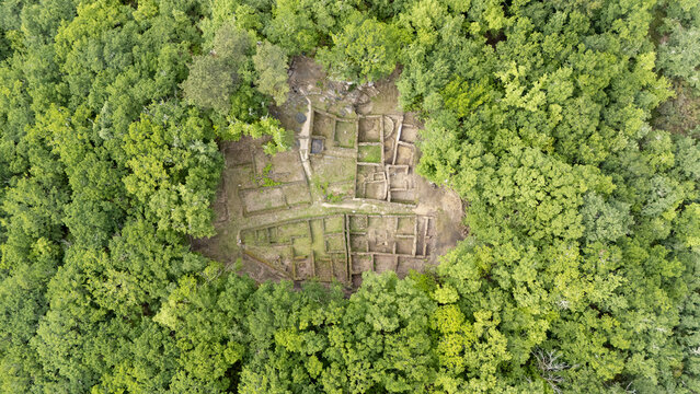 Aerial view of the stone foundations and ancient ruins of Castro de Armea surrounded by dense green forest in Allariz, Province of Ourense, Spain.