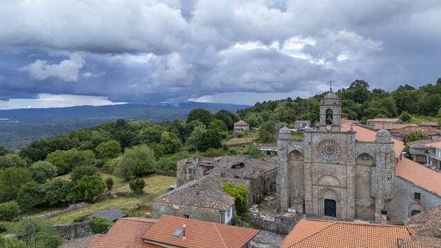 Aerial view of Iglesia de Santa Marina de Augas Santas with its stone facade and bell tower surrounded by traditional houses and lush green forests Augas Santas, Ourense, Spain.