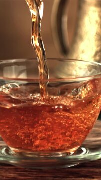 A super slow motion jet of tea pours into a cup of air bubbles. On a brown background. Filmed on a high-speed camera at 1000 fps.