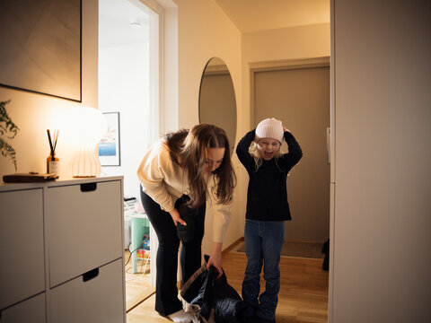 Playful girl standing beside mother picking up jacket from floor at corridor of house
