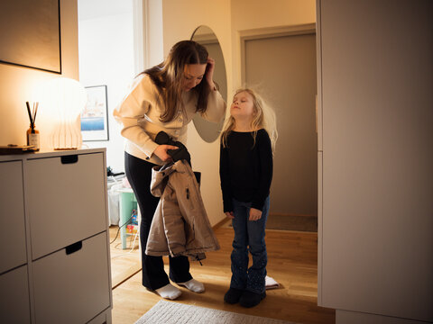Mischievous girl standing near mother holding jacket while standing at corridor of house