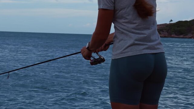 Rear View of Young Woman Holding Spinning Rod Near Tropical Coastline and Dark Ocean Water, Slow Motion Fishing and Outdoor Adventure