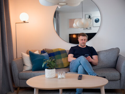 Man using smart phone while sitting with legs crossed at knee on sofa at home