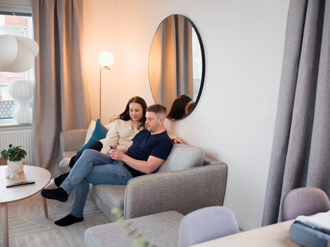 High angle view of man and woman spending leisure time using smart phone while sitting on sofa at home