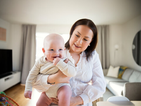 Mother carrying cute male toddler while standing in home