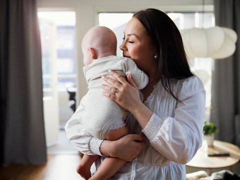 Affectionate mother embracing toddler son while standing in home