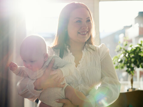 Sunlight shining through window of home while smiling mother standing with cute toddler son
