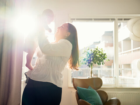 Happy mother playing with baby boy in brightly lit home