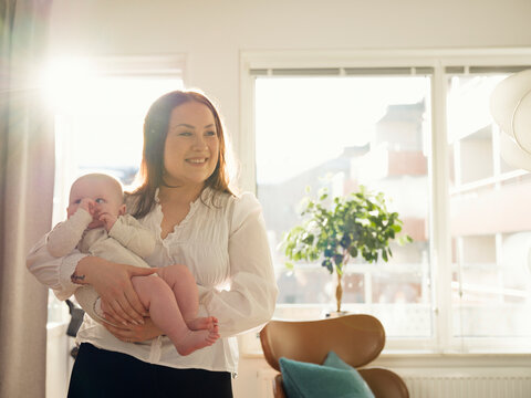 Smiling woman spending leisure time with cute baby boy at home on sunny day