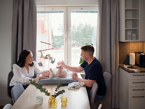 Parents spending leisure time with baby boy lying on small bed in home