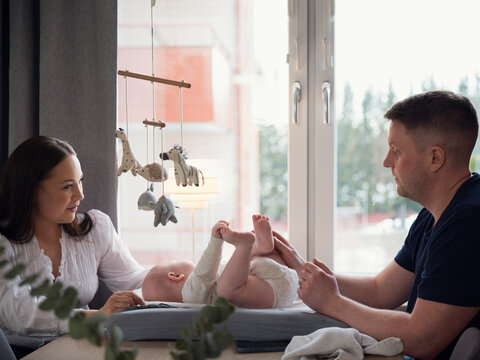 Parents spending leisure time with toddler son lying on small bed in home