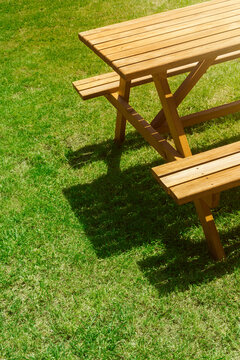 High-angle shot of a wooden picnic table and bench on a vibrant green lawn. Sunny outdoor lifestyle background with strong shadows, large copy space for text, weekend leisure, and park furniture