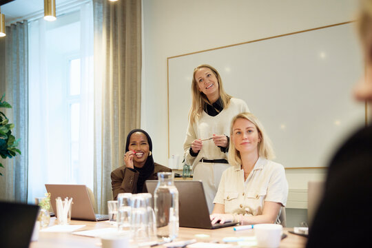 Happy businesswomen interacting with colleagues in office meeting