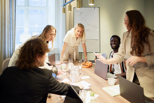 Group of diverse entrepreneurs discussing strategies while standing around illuminated table in office