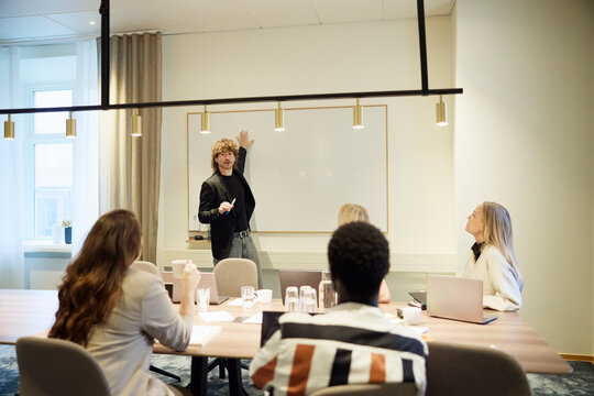 Male entrepreneur explaining strategies to coworkers sitting in meeting room