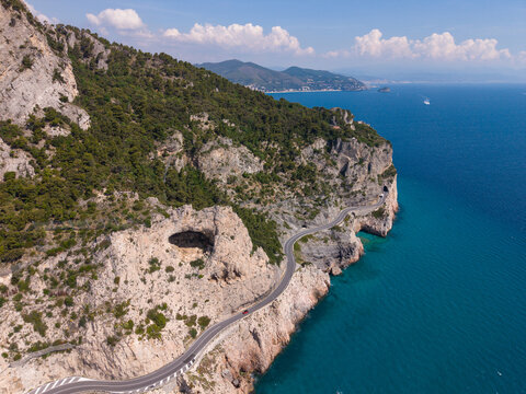 Aerial view of the Sentiero del Pellegrino area featuring the winding coastal road along steep limestone cliffs and the turquoise sea in Noli, Liguria, Italy.