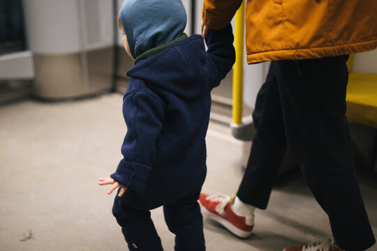 Toddler boy holding hands of his father while walking inside train