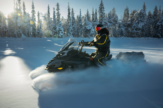 Rider in black winter suit driving snowmobile on snowy plain